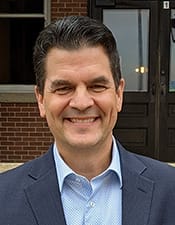 Photo of Provost DeRochi smiling wearing a blue suit jacket and light blue collared shirt