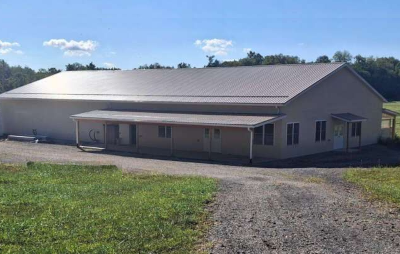 Agricultural innovation center building with light tan exterior metal roof and covered entry surrounded by gravel driveway and green grass under clear blue sky with trees in the background