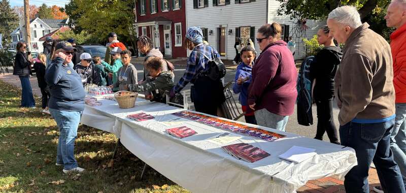 A long table filled with books, pamphlets, and water is manned by a Shepherd University professor. A line of 12-15 people peruses its contents.