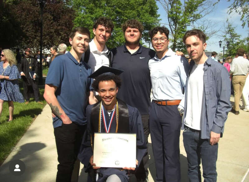 Members of a fraternity dressed up stand behind their fraternity brother dressed in graduation cap and gown holding his ϳԹdiploma