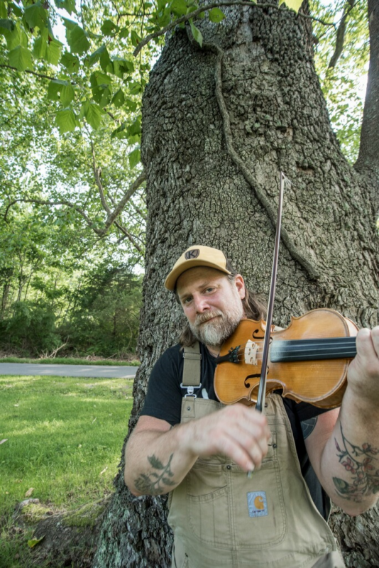 Ben Townsend playing fiddle in front of a large tree on a sunny day in Shepherdstown, West Virginia