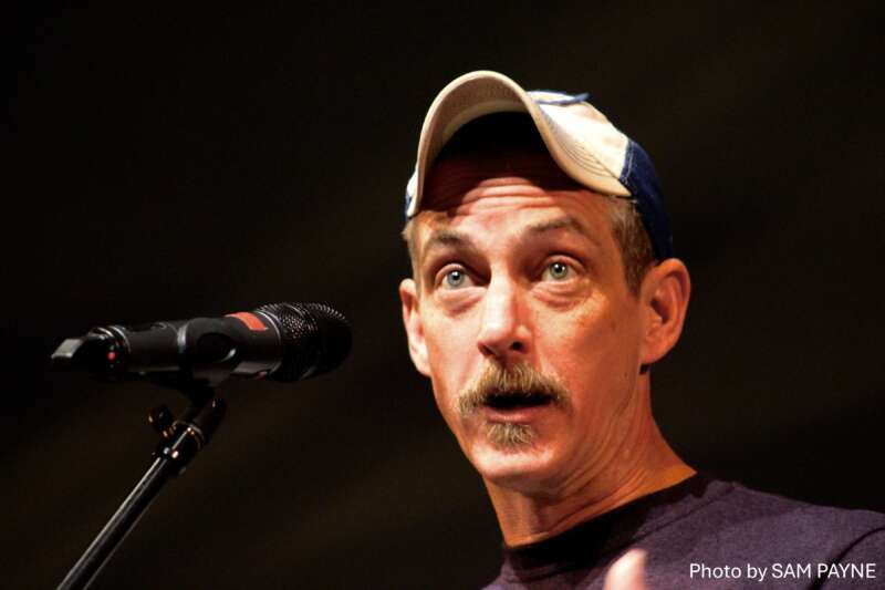 Storyteller Bil Lepp speaking into a microphone on stage, wearing a baseball cap – photo by Sam Payne