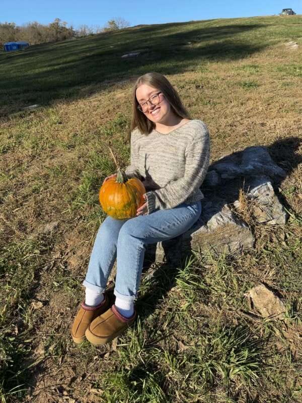 Young woman sitting on a lawn holding a pumpkin.