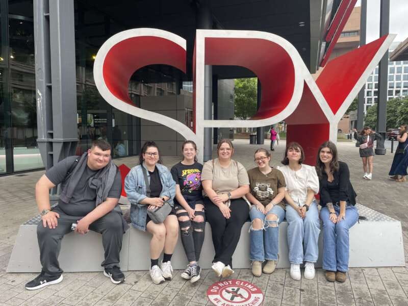 Group of people sitting outside in front of a SPY sign.