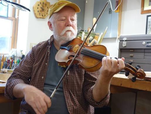 Fiddler Dave Bing wearing baseball cap plays a fiddle he made
